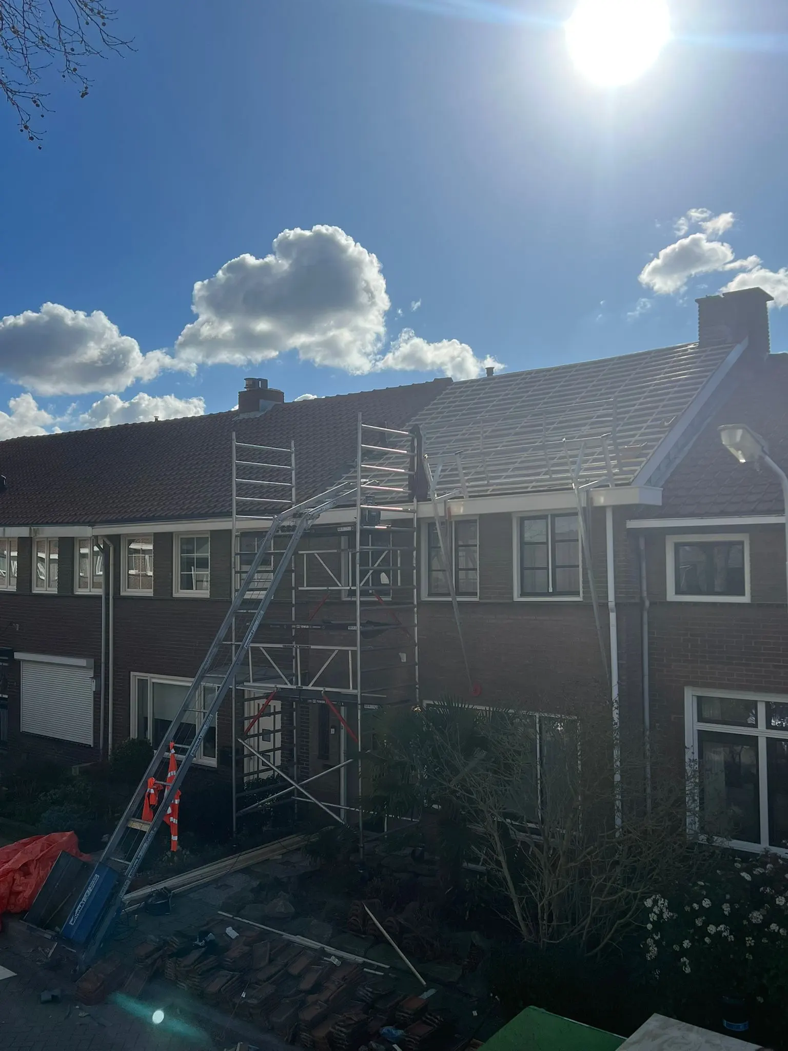Pannendak in uitvoering met zichtbare panlatten, steiger en ladderlift in een straat met rijtjeshuizen