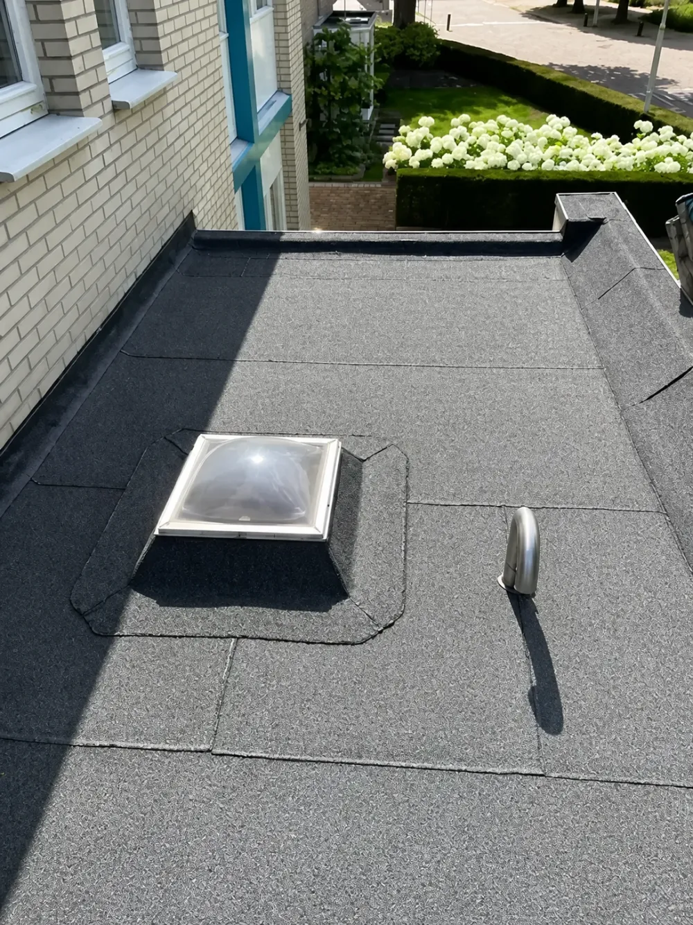Na: hetzelfde plat dak met nieuwe grijze dakbedekking, lichtkoepel en ontluchtingspijp