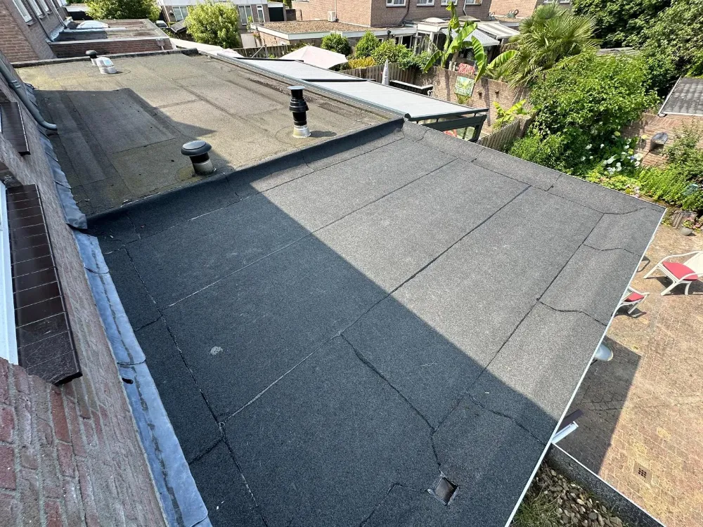 Nieuw donker plat dak naast een ouder dak, gezien vanuit de achtertuin